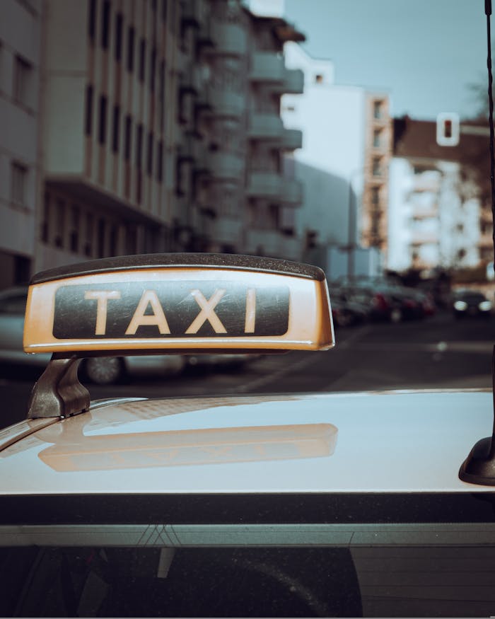Close-up of a taxi sign on a car with city buildings in the background.